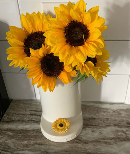 White ceramic Nora Fleming utensil holder with sunflower decoration holding bright yellow sunflowers on marble countertop